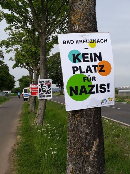 Ein Plakat mit der Aufschrift „Kein Platz für Nazis“ hängt an einem Baum am Radweg in der Nähe des Mahnmals „Feld des Jammers“ in Bretzenheim.